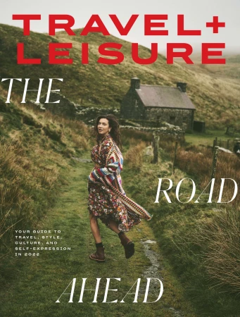 Magazine cover featuring a woman in a floral dress walking on a path in a rural landscape with a stone building in the background.