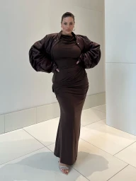 Plus size woman in a dark brown dress and jacket posed against a plain tiled wall