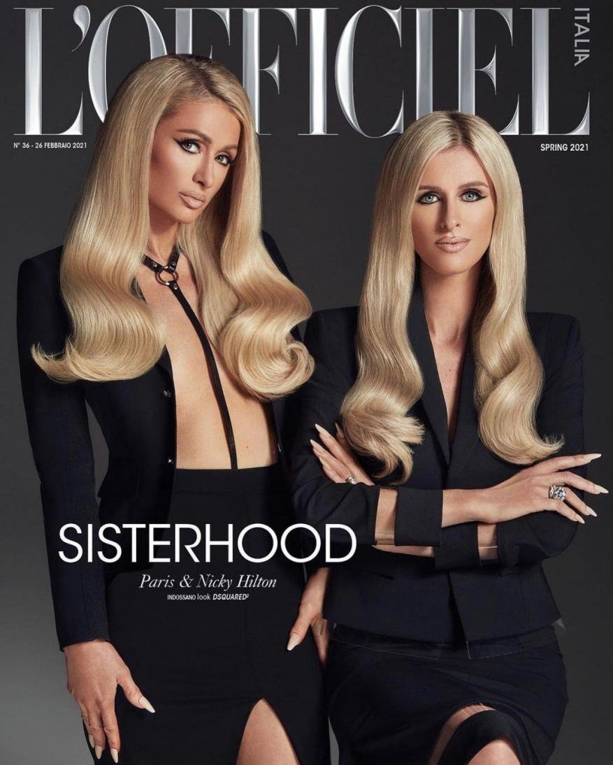 Paris and Nicky Hilton pose for L'Officiel Italia magazine cover, wearing black blazers, long blonde wavy hair, and standing indoors.
