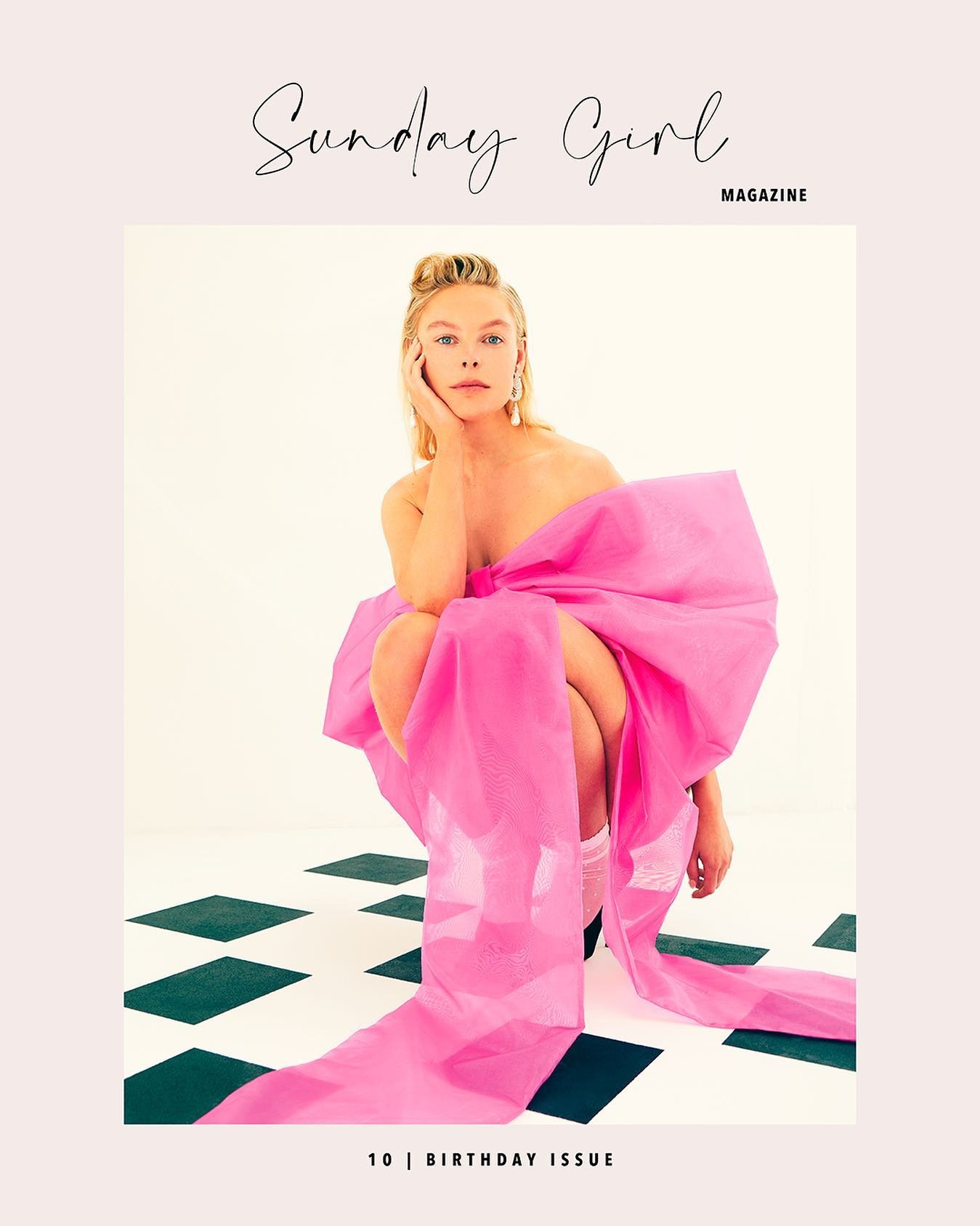 Blonde woman poses wrapped in a large pink bow, seated on a black and white checkered floor, for a Sunday Girl magazine cover.