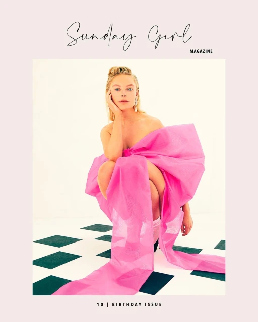 Blonde woman poses wrapped in a large pink bow, seated on a black and white checkered floor, for a Sunday Girl magazine cover.