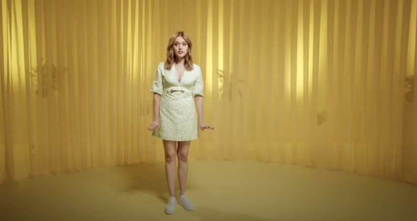 Full-length shot of adult female in floral dress and white sneakers against yellow draped backdrop in brightly lit photo studio.