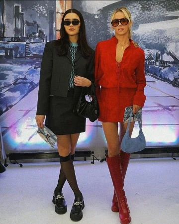 Two women wearing sunglasses and stylish outfits posing together against a textured artistic backdrop in London