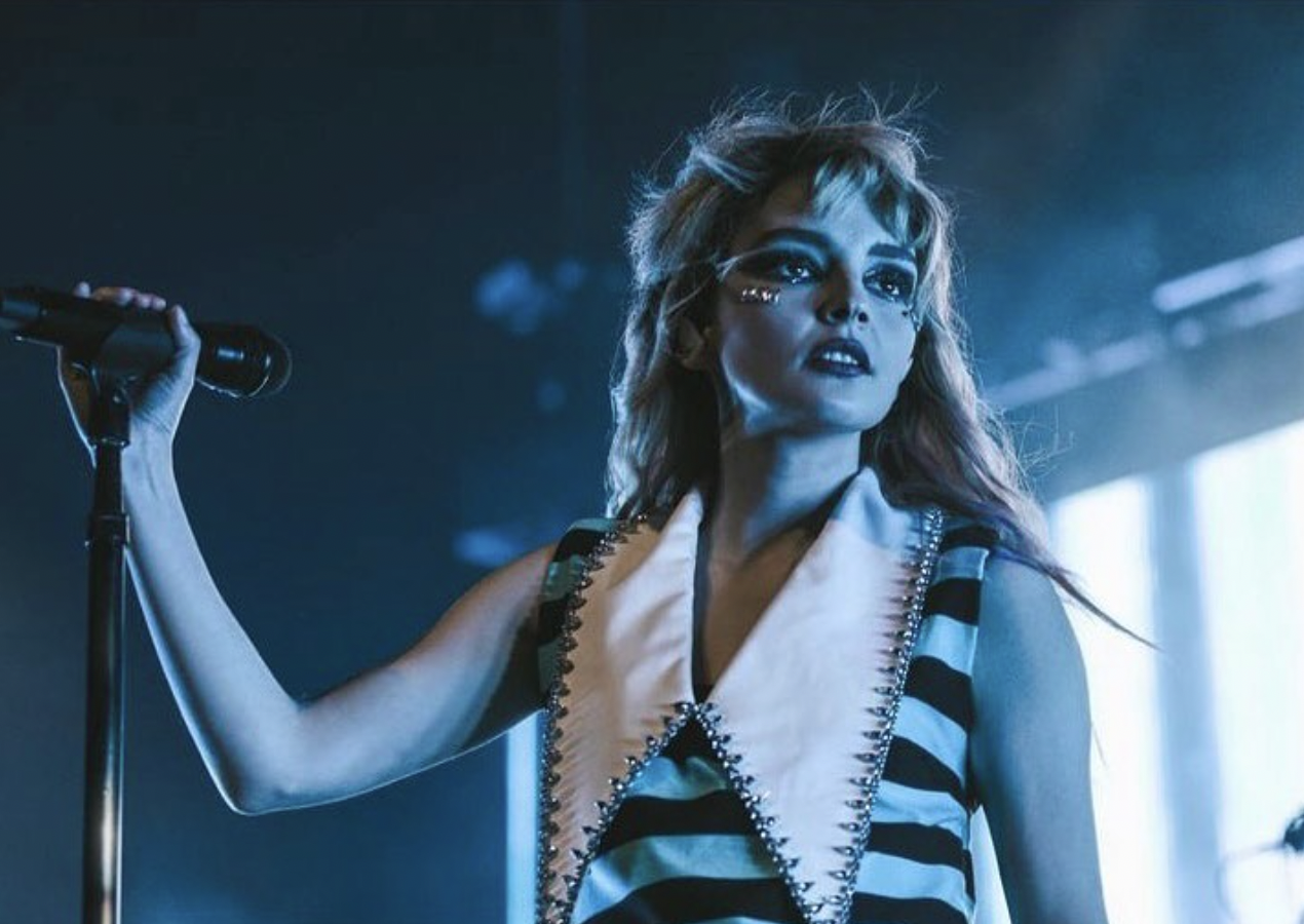 Singer performs on stage with makeup, striped top, and microphone. Woman with a microphone performing on stage in a blue light.
