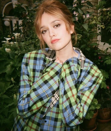 Woman with auburn hair wearing a blue and green plaid blazer standing outdoors among leafy green plants styled by Emma Lane