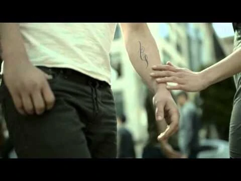 Close-up of a person reaching out to touch another person's tattooed forearm in an urban street setting.