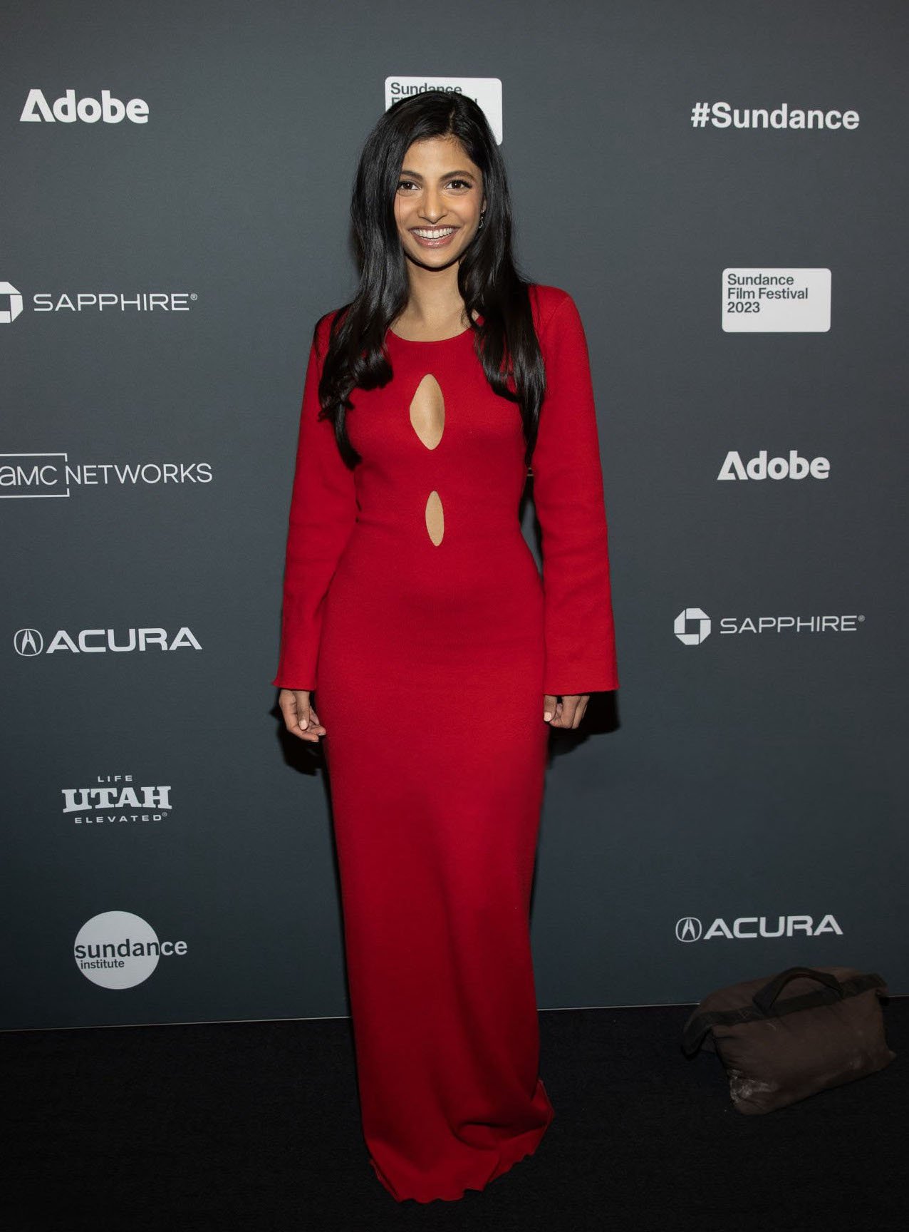 Woman in a red dress poses on a branded backdrop at the Sundance Film Festival 2023, smiling and looking at the camera.