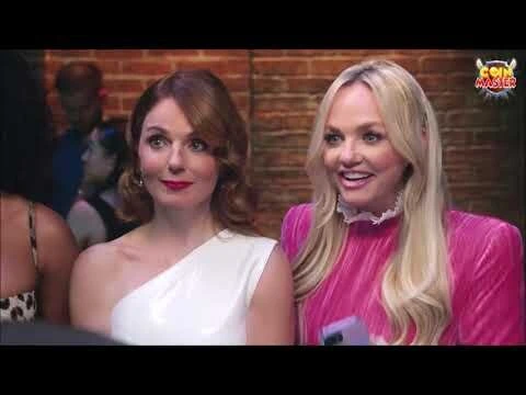 Two adult women pose indoors at an event, one in a white dress and the other in pink, with a brick wall background.