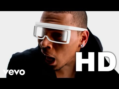 Close-up of adult male wearing white futuristic visor-like glasses in front of a white background with prominent HD and Vevo logos.