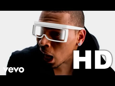 Close-up of adult male wearing white futuristic visor-like glasses in front of a white background with prominent HD and Vevo logos.