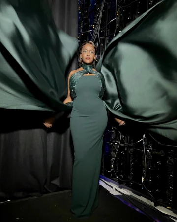 Elegant woman in a green gown with a shimmering bodice, captured in a medium shot against a backstage environment with lighting cables.