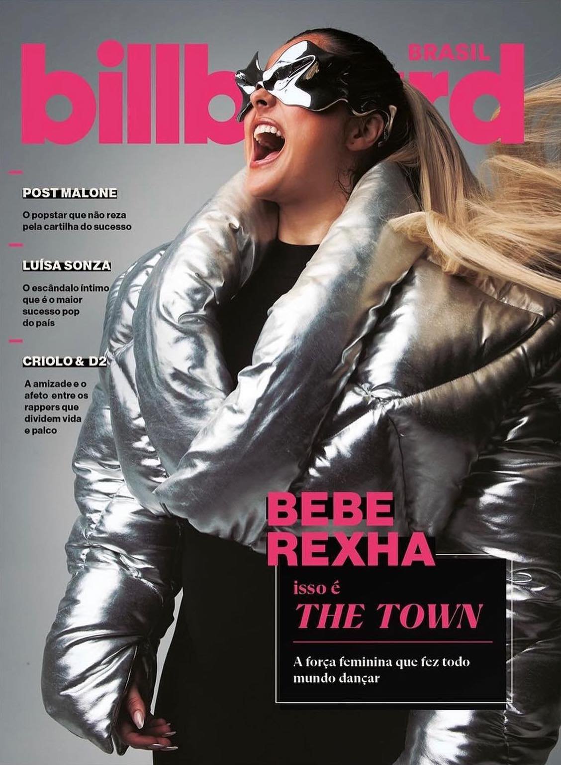 Bebe Rexha on Billboard Brasil magazine cover. She wears a silver puffy jacket and futuristic silver glasses against a pink background.