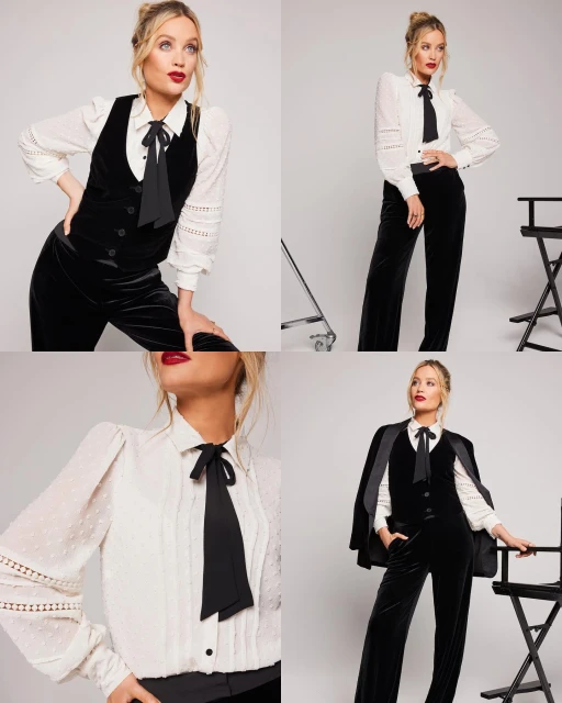 A woman with blonde hair is wearing a black velvet vest, a white shirt with a bow, and black pants. The background is a light grey.