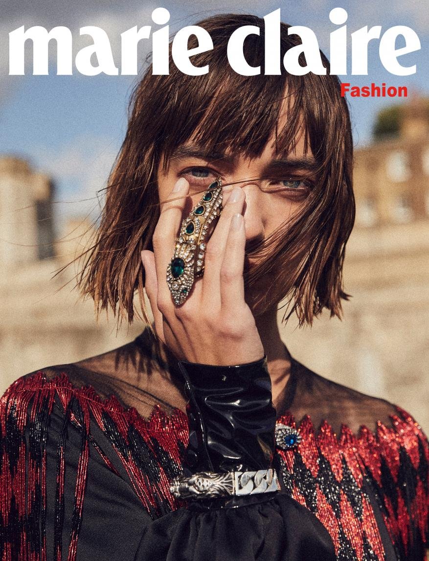 Marie Claire magazine cover featuring a woman with short brown hair wearing a black dress with a jeweled ring and bracelet against a stone background.