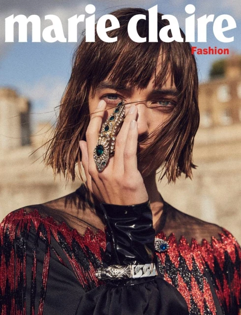 Marie Claire magazine cover featuring a woman with short brown hair wearing a black dress with a jeweled ring and bracelet against a stone background.