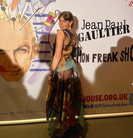 Woman in printed sleeveless dress standing in front of Jean Paul Gaultier Fashion Freak Show backdrop
