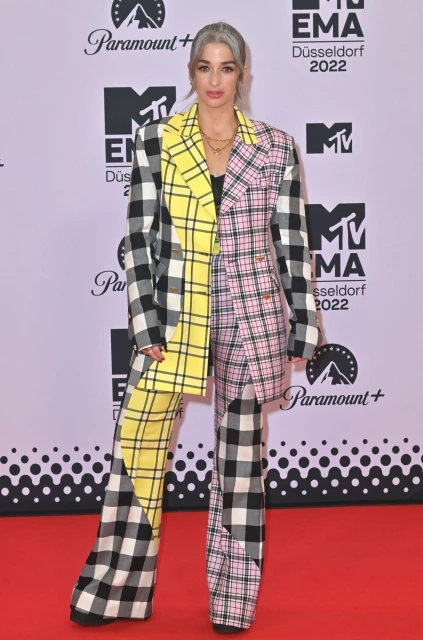 Adult female in patterned pantsuit attends the 2022 MTV Europe Music Awards in Düsseldorf, Germany, against a branded lavender backdrop.
