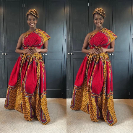 Black woman wearing a red and yellow patterned one-shoulder dress with braided updo hair standing indoors