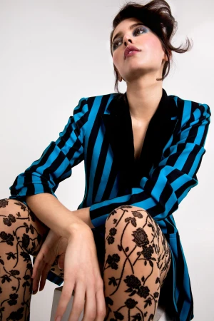 Model in blue and black striped blazer wearing patterned tights against a white background