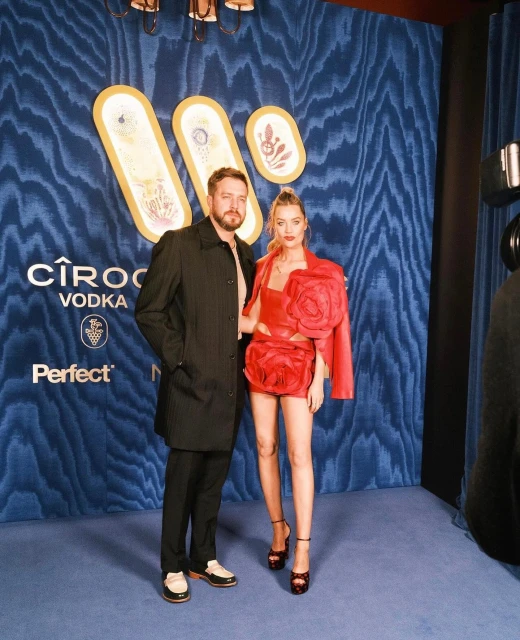 Man and woman pose on blue patterned backdrop promoting Ciroc Vodka. The woman wears a red dress with floral accents.