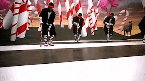 Group of adult male performers with candy cane props in a whimsical stage setting with white and red candy cane decorations.