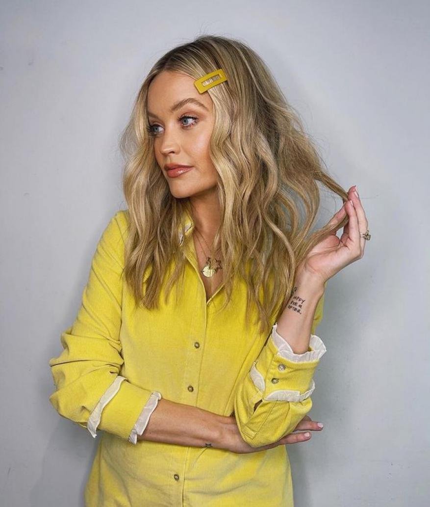 Blonde woman with yellow hair clip and yellow shirt in a medium shot against a light-grey backdrop in a studio setting.