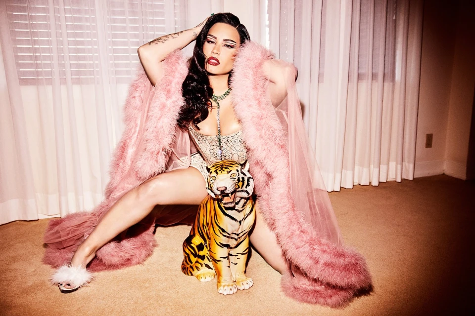 Adult female in lingerie and pink robe poses with a decorative tiger in an indoor setting with window blinds and peach carpet.