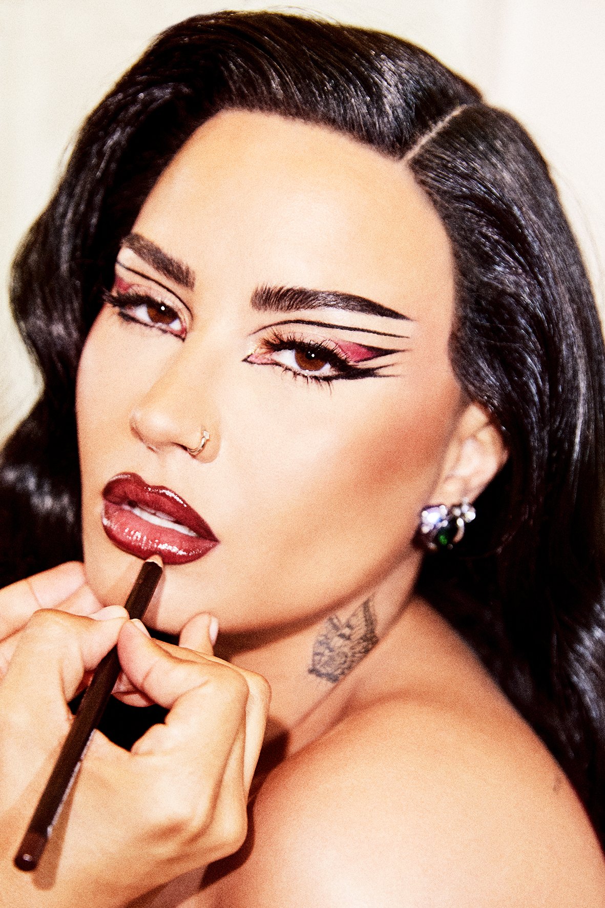Close-up of an adult female getting her makeup applied, focusing on her bold graphic eyeliner and deep red lip color.
