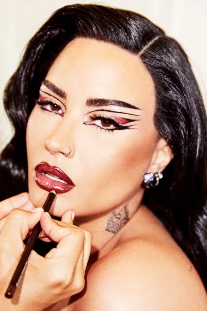 Close-up of an adult female getting her makeup applied, focusing on her bold graphic eyeliner and deep red lip color.