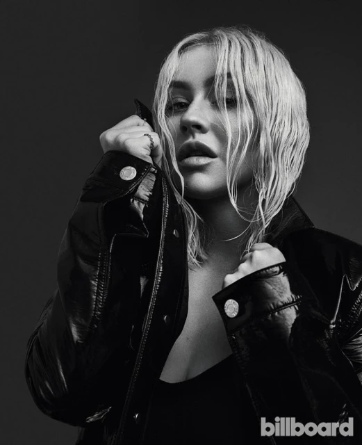 Black-and-white headshot of Christina Aguilera wearing a black jacket. She is looking at the camera with a slight smile.