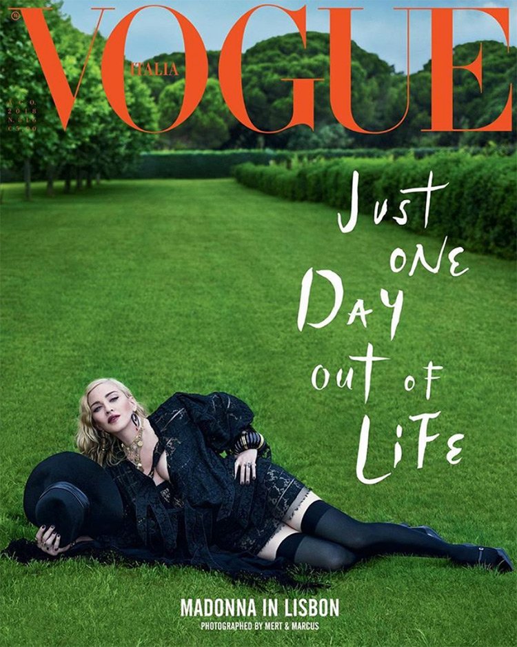 Vogue Italia magazine cover featuring Madonna lying on green grass in a black dress and hat, with a background of trees and greenery.