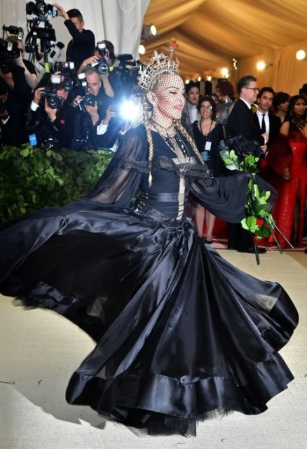Madonna at a celebrity event, twirling in a black dress with a bouquet of black roses, surrounded by photographers with flash photography.