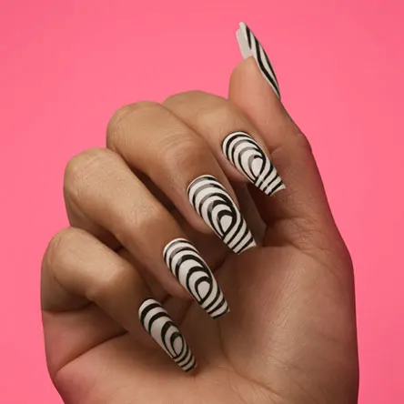 Hand displaying long, coffin-shaped nails with a black and white concentric circle design against a bright pink background.