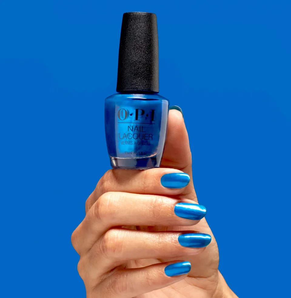 Close-up of a hand holding a bottle of OPI blue nail lacquer against a vibrant blue background, showcasing a beauty and fashion concept.