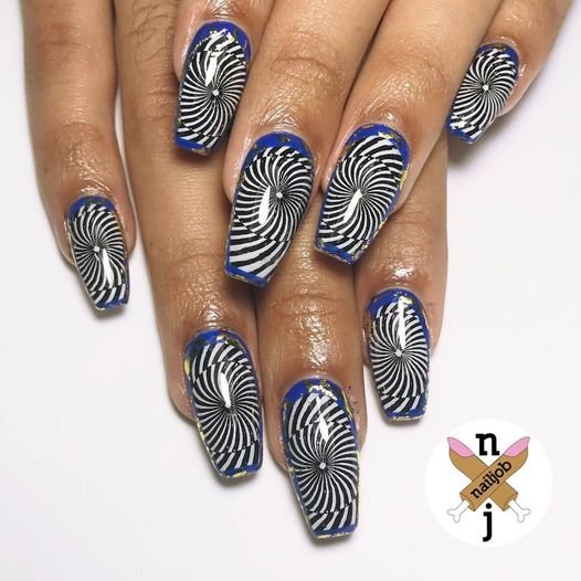 Close-up on a woman's hands featuring long, coffin-shaped nails with a blue base and a black and white spiral design. Beauty shot.