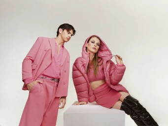 Man in pink suit and woman in pink puffer jacket with black boots in a studio