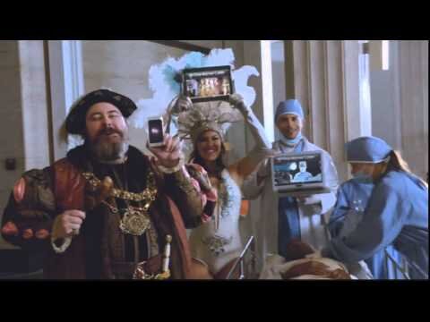 People in costumes hold up electronic devices in an indoor setting, mixing historical and modern elements in a visually striking image.