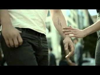 Close-up of a person reaching out to touch a man's tattooed forearm in an urban street setting.