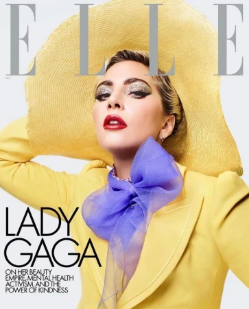 Elle magazine cover featuring Lady Gaga wearing a yellow hat and blazer with a purple scarf, posing in a photo studio.