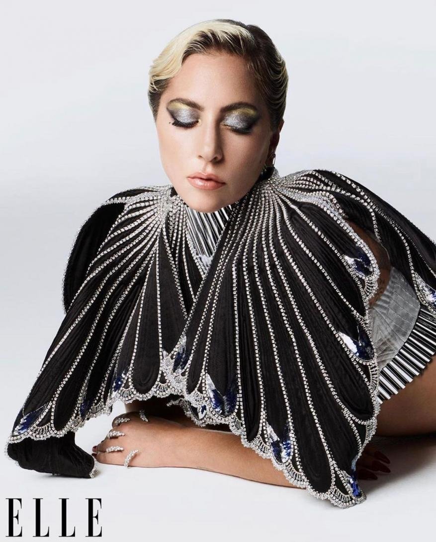 Close-up portrait of a woman with platinum blonde hair, wearing a black jeweled dress, against a seamless studio backdrop.