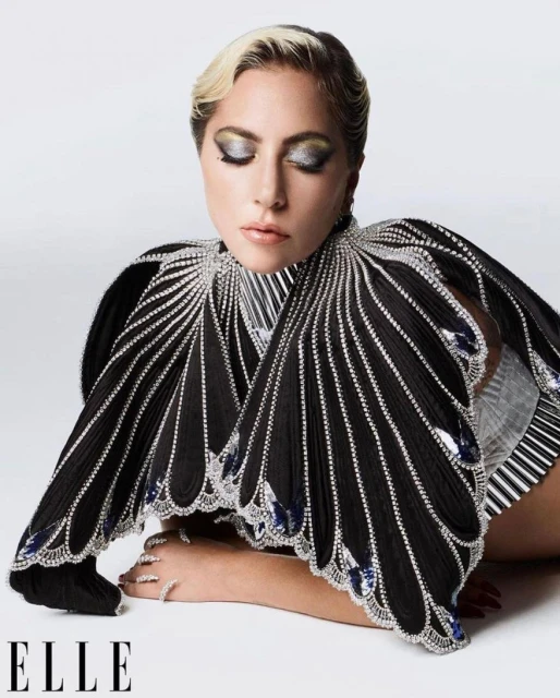 Close-up portrait of a woman with platinum blonde hair, wearing a black jeweled dress, against a seamless studio backdrop.