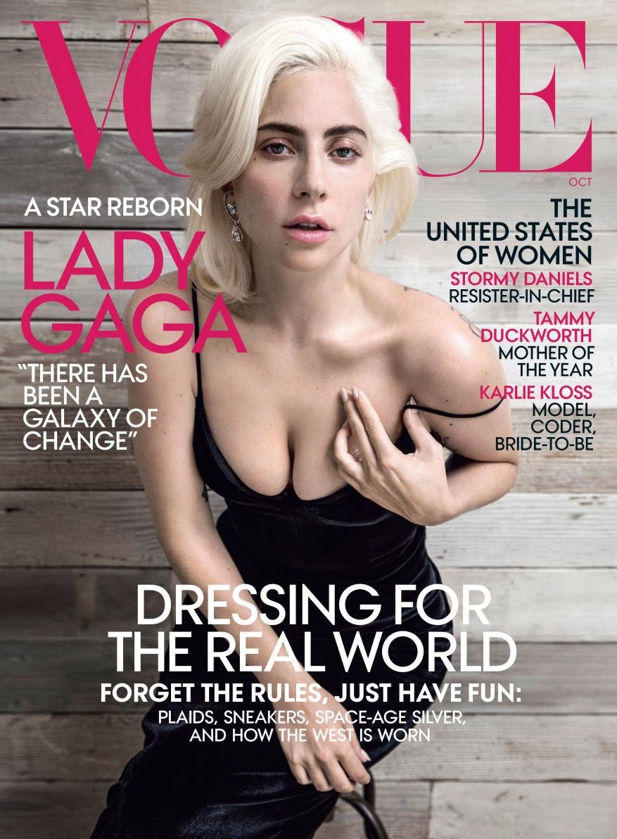 Vogue magazine cover featuring Lady Gaga in a low-cut black dress with a weathered wood plank background and pink Vogue logo.