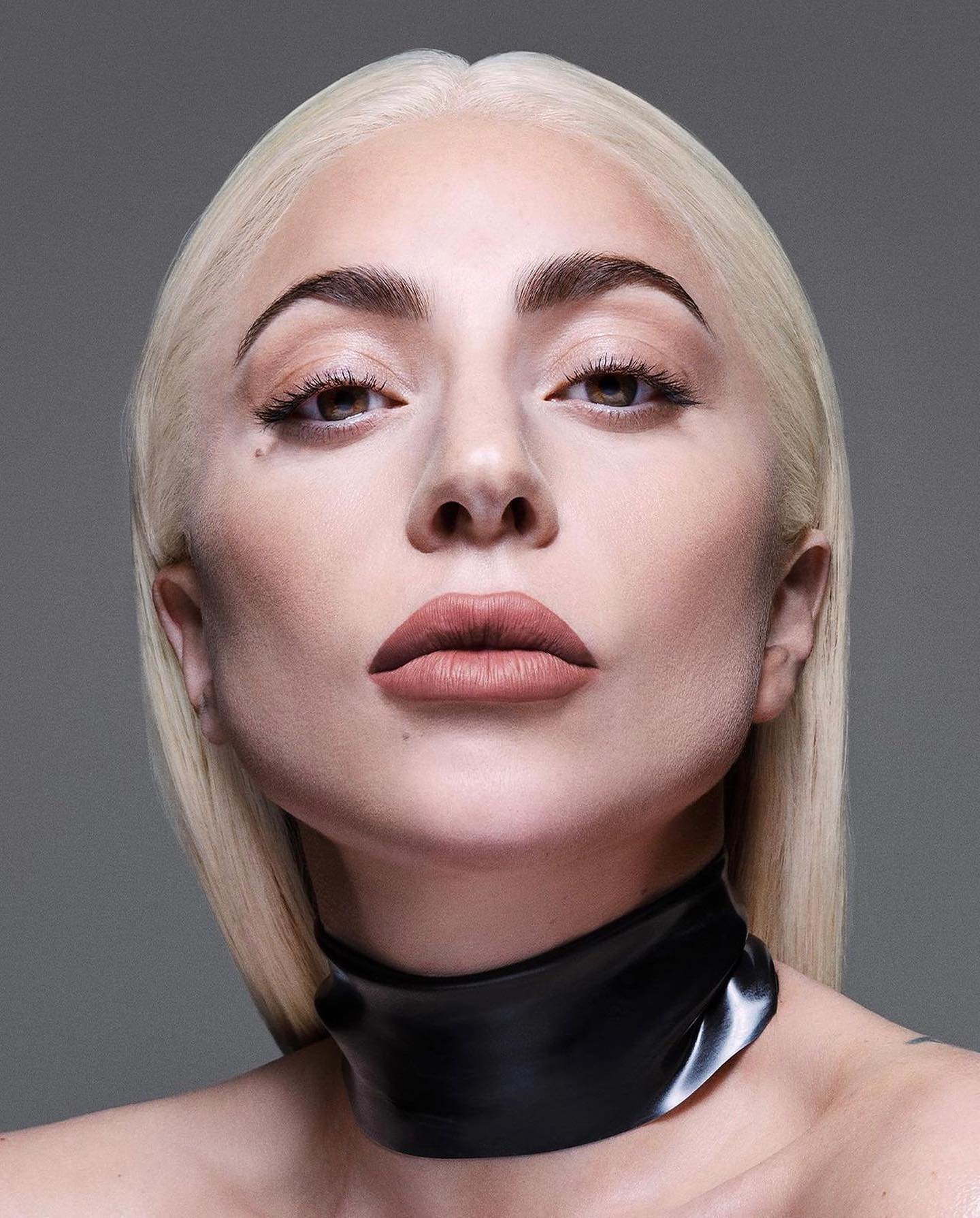 Close-up portrait of an adult female with blonde hair, light skin, and a black choker, set against a solid gray background in a photo studio.