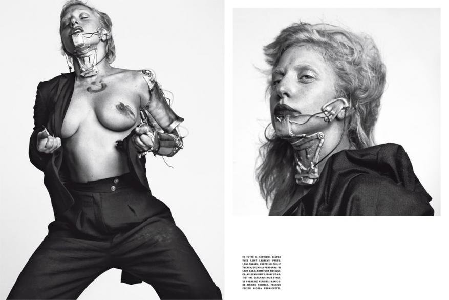 Avant-garde fashion shot featuring a woman with chest bared, metal prosthetic additions, styled dark suit, set against a light backdrop.