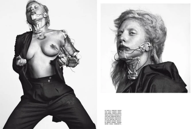 Avant-garde fashion shot featuring a woman with chest bared, metal prosthetic additions, styled dark suit, set against a light backdrop.