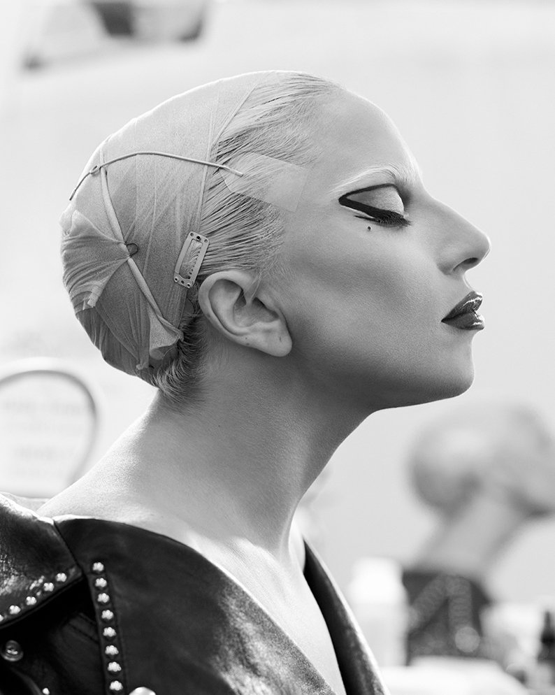 Black-and-white portrait of a fair-skinned woman with dark eye makeup, wearing a studded leather jacket, her eyes closed, and head wrapped.