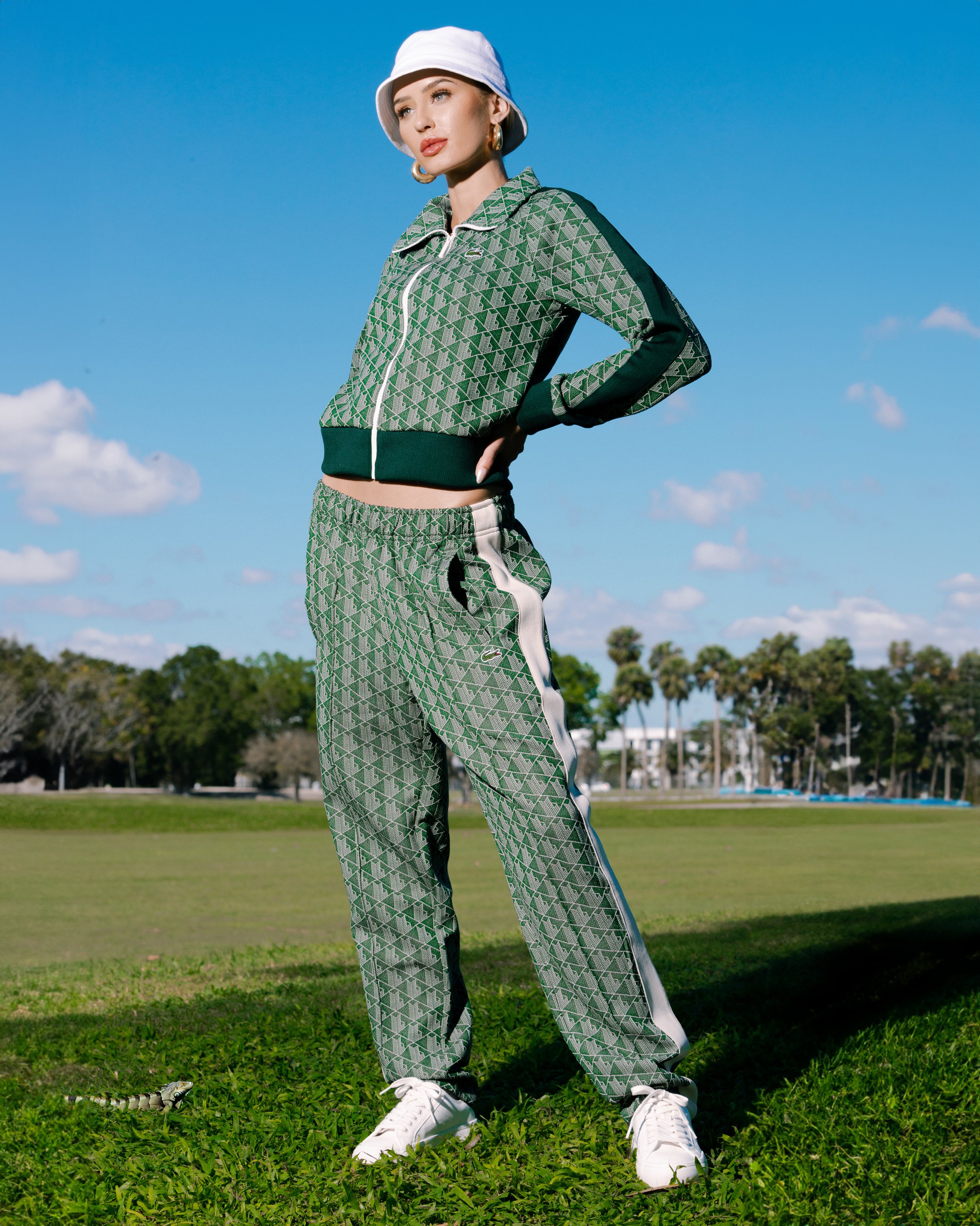 Woman in patterned tracksuit poses in sunny outdoor setting with blue sky, showcasing casual fashion and style against a natural backdrop.