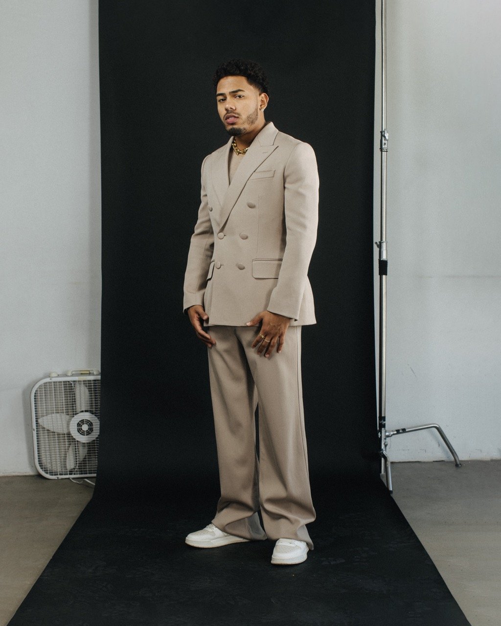 Stylish adult male poses in a beige suit with neutral background, studio lighting, and white sneakers for a contemporary fashion shoot.