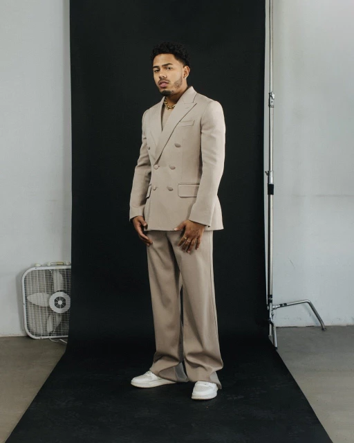 Stylish adult male poses in a beige suit with neutral background, studio lighting, and white sneakers for a contemporary fashion shoot.