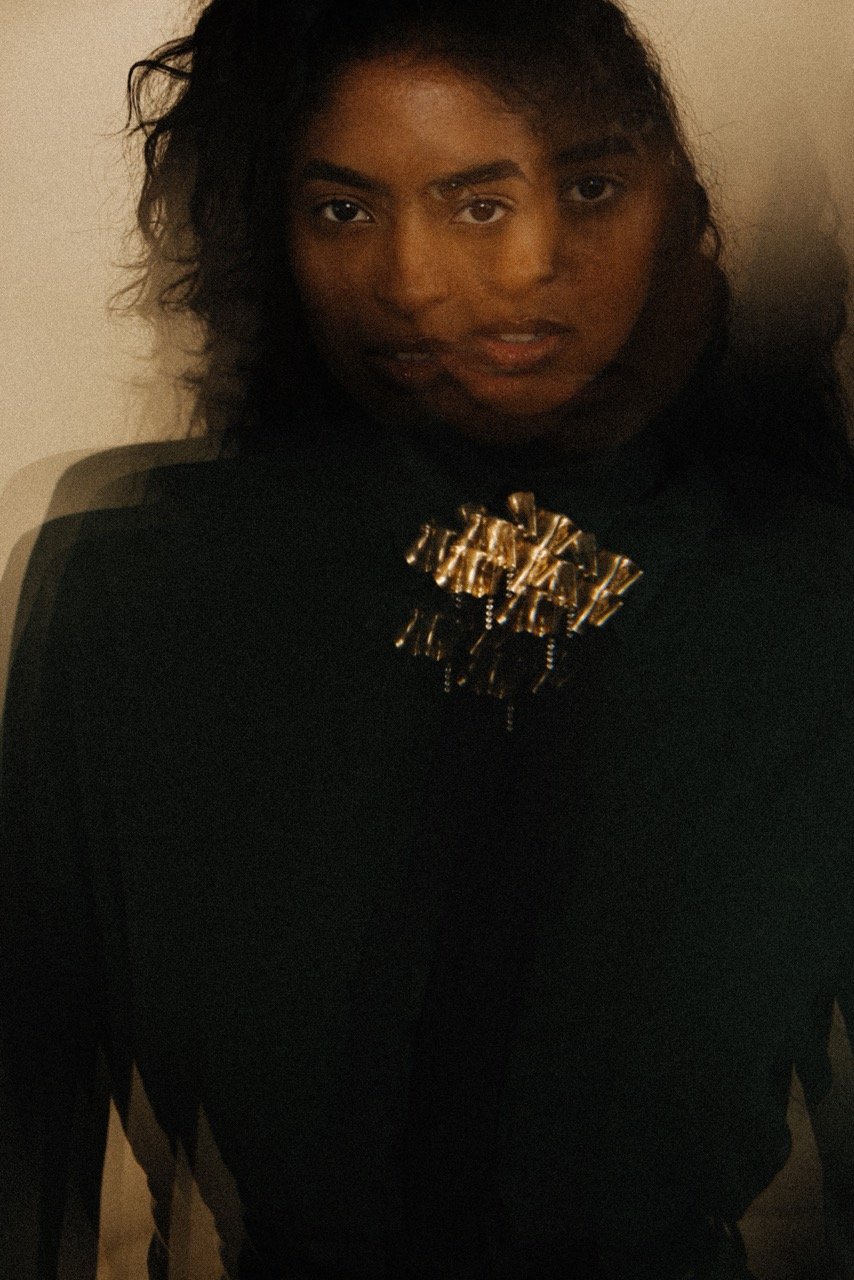 Portrait of an adult woman with dark hair wearing a dark green top with a gold and black brooch, long exposure and motion blur. 